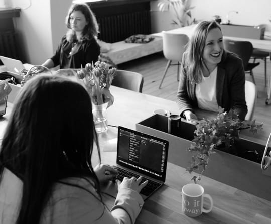 Three women sitting around a table with laptops, most likely learning front end development.